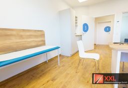 Ansicht Richtung Tür im Behandlungszimmer – im Fokus die hellblaue Liege und Raumbeschriftungen an den Türen.