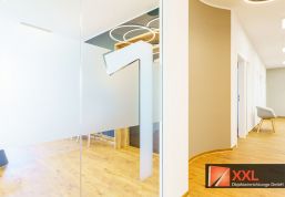 Die moderne Glastür mit großer, stilisierter Nummer „1“ markiert den Zugang zum Wartezimmer. Die helle, freundliche Flurgestaltung mit organischen Formen und geschwungenen Linien schafft bereits beim Betreten eine ruhige und angenehme Atmosphäre.
