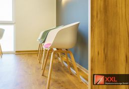 Die seitliche Perspektive zeigt die klare Linienführung und hochwertige Verarbeitung der Möbel. Die schlichten, ergonomischen Stühle mit gepolsterten Sitzflächen in dezenten Farbtönen sind nicht nur optisch ansprechend, sondern bieten auch hohen Sitzkomfort.