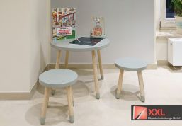 Ein Kinderbereich mit einem kleinen Spieltisch in Mintgrün und passenden Hockern. Kindgerechte Spiele und Bücher laden zum Verweilen ein und machen den Apothekenbesuch angenehmer für die Kleinen.