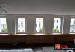 Gesamtansicht der durchgehenden Schrankzeile, die sich unter der gesamten Fensterfront des Altbauzimmers entlangzieht.