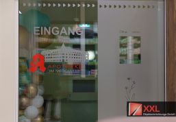 Gläserne Eingangstür: Klare Linien und modernes Design – die gläserne Eingangstür mit Logo und Öffnungszeiten sorgt für Transparenz und einen offenen Empfangsbereich.