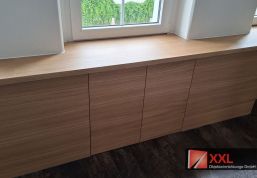Maßgefertigtes Sideboard mit grifflosen Fronten, das nahtlos in die durchgehende Fensterbank in Holzoptik übergeht.