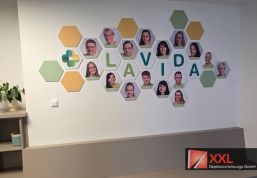 Teamwand aus Wabenelementen in den Hausfarben mit den Porträts der Mitarbeitenden als Blickfang im Eingangsbereich.