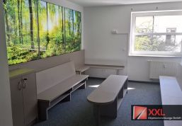 Wartebereich mit hinterleuchtetem Waldmotiv, durchgehender Sitzbank und kleiner Kinderecke.